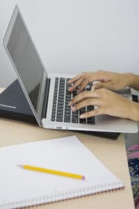 Hands at a laptop keyboard with notepad nearby