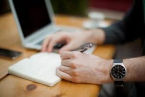 Person writing in a notebook next to a laptop computer